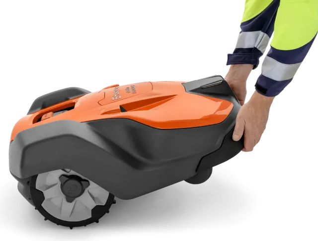 Людина, яка тримає в руках роботизовану газонокосарку Husqvarna, демонструє її конструкцію.